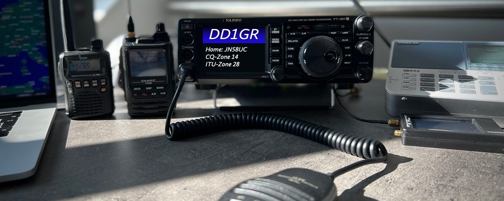 A QSL-Card from DD1GR showing FT-991A with a Mic in front as well as an FT3D and a R3 and the edge of a laptop